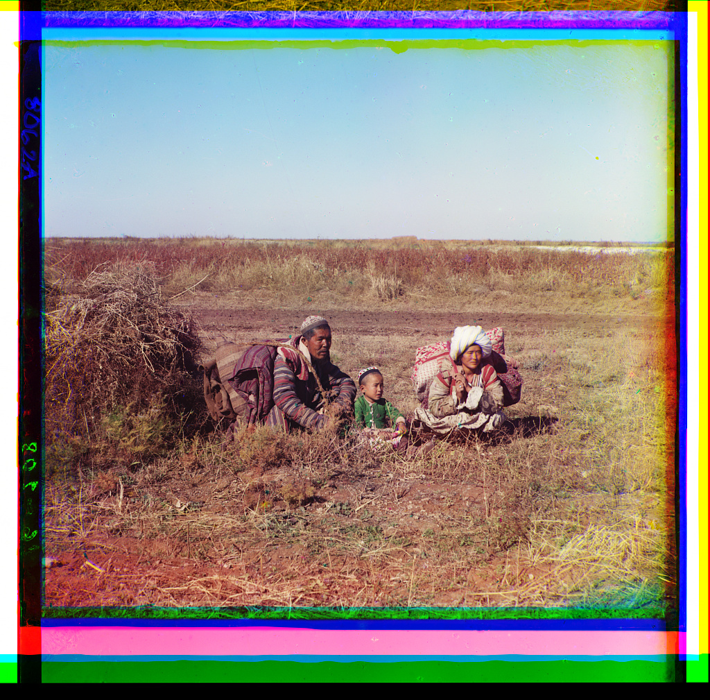 Two Kazakh parents and their child sit among the fields.