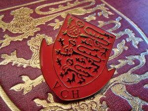 Enamel badge in red and gold showing the three lions passant of the Victoria County History logo with the initials VCH below