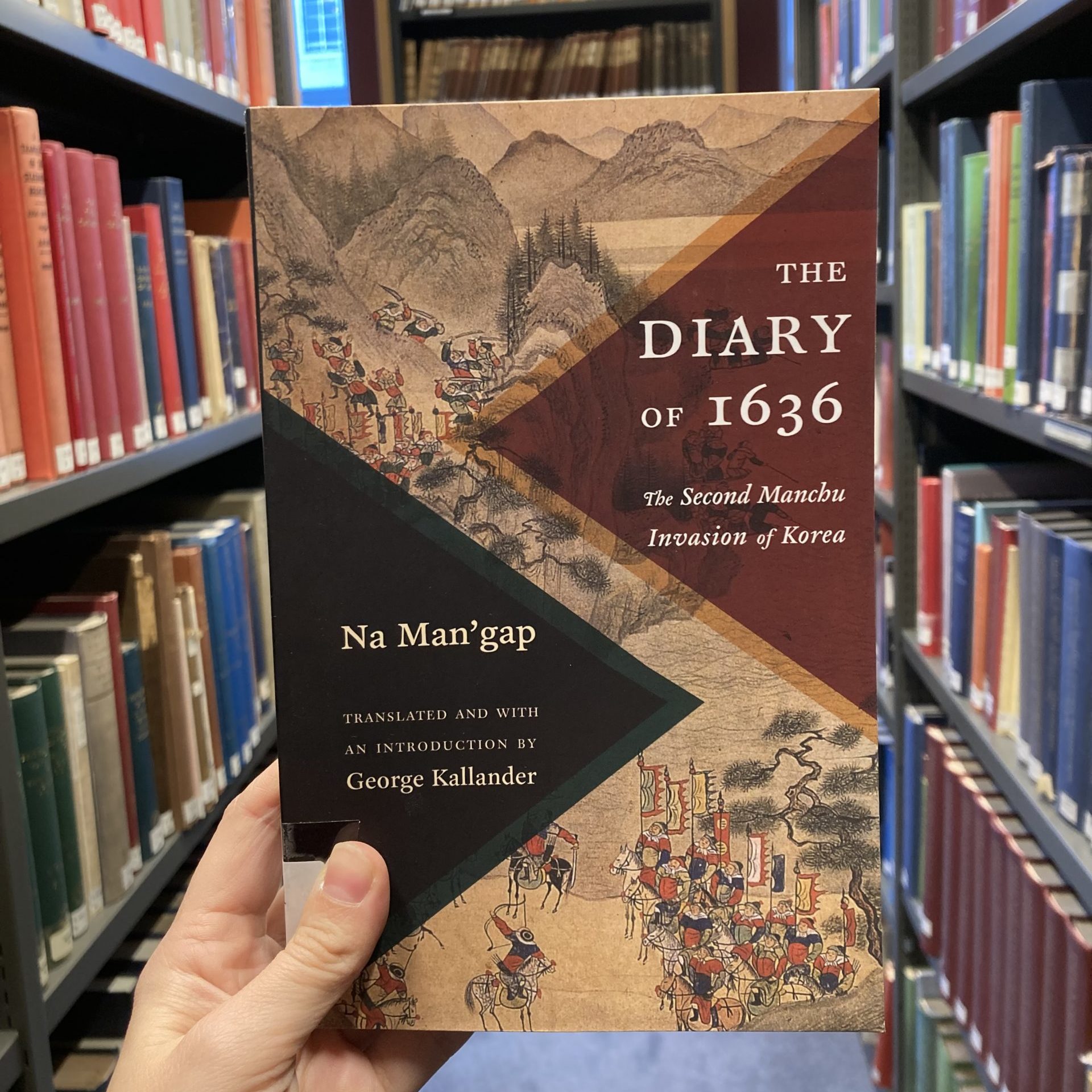 A view of the front cover of 'The Diary of 1636: The second Manchu invasion of Korea' being held up in between two bookcases