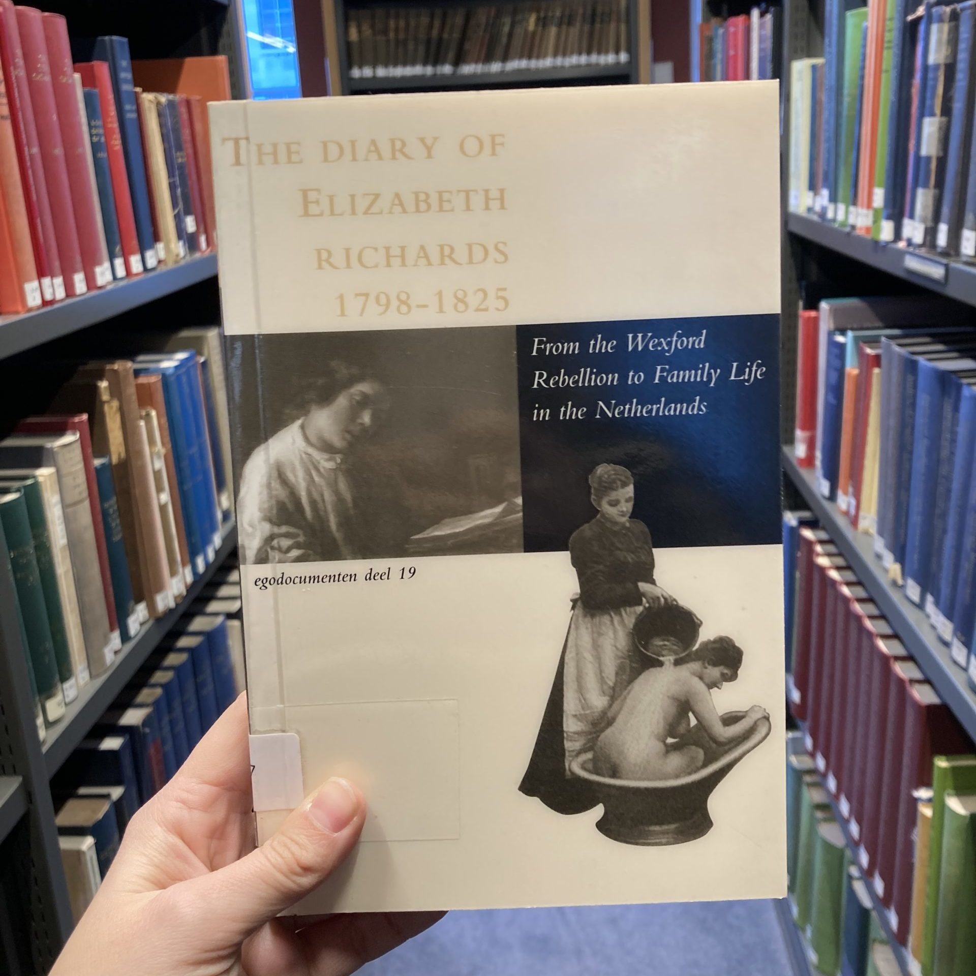 A view of the front cover of 'The Diary of Elizabeth Richards' being held up in between two bookcases