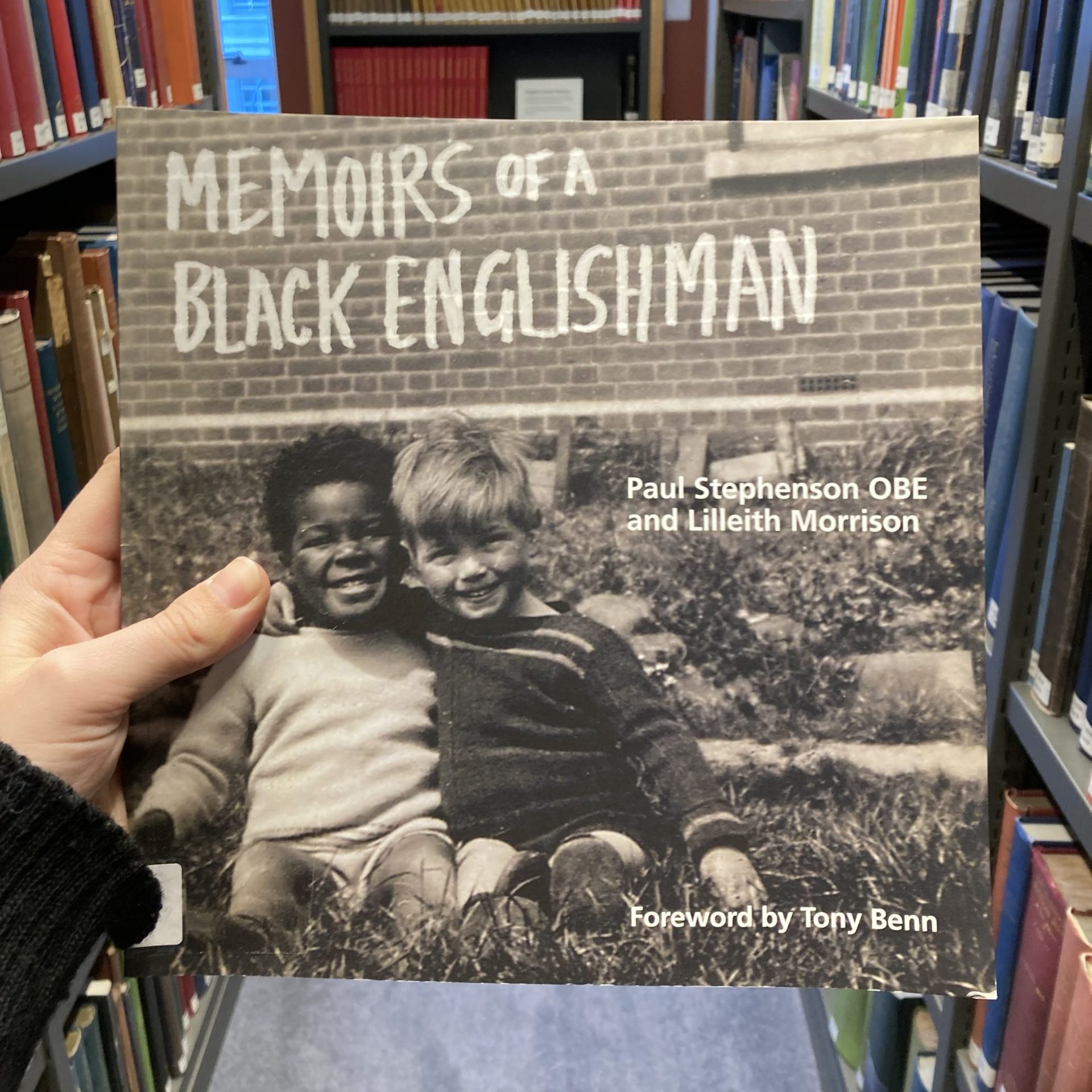 A view of the front cover of 'Memoirs of a Black Englishman' being held up in between two bookcases